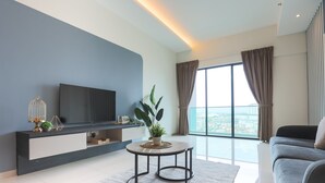 Una sala de estar moderna con un televisor de pantalla plana, una mesa de centro redonda, un sofá gris y un ventanal con cortinas.