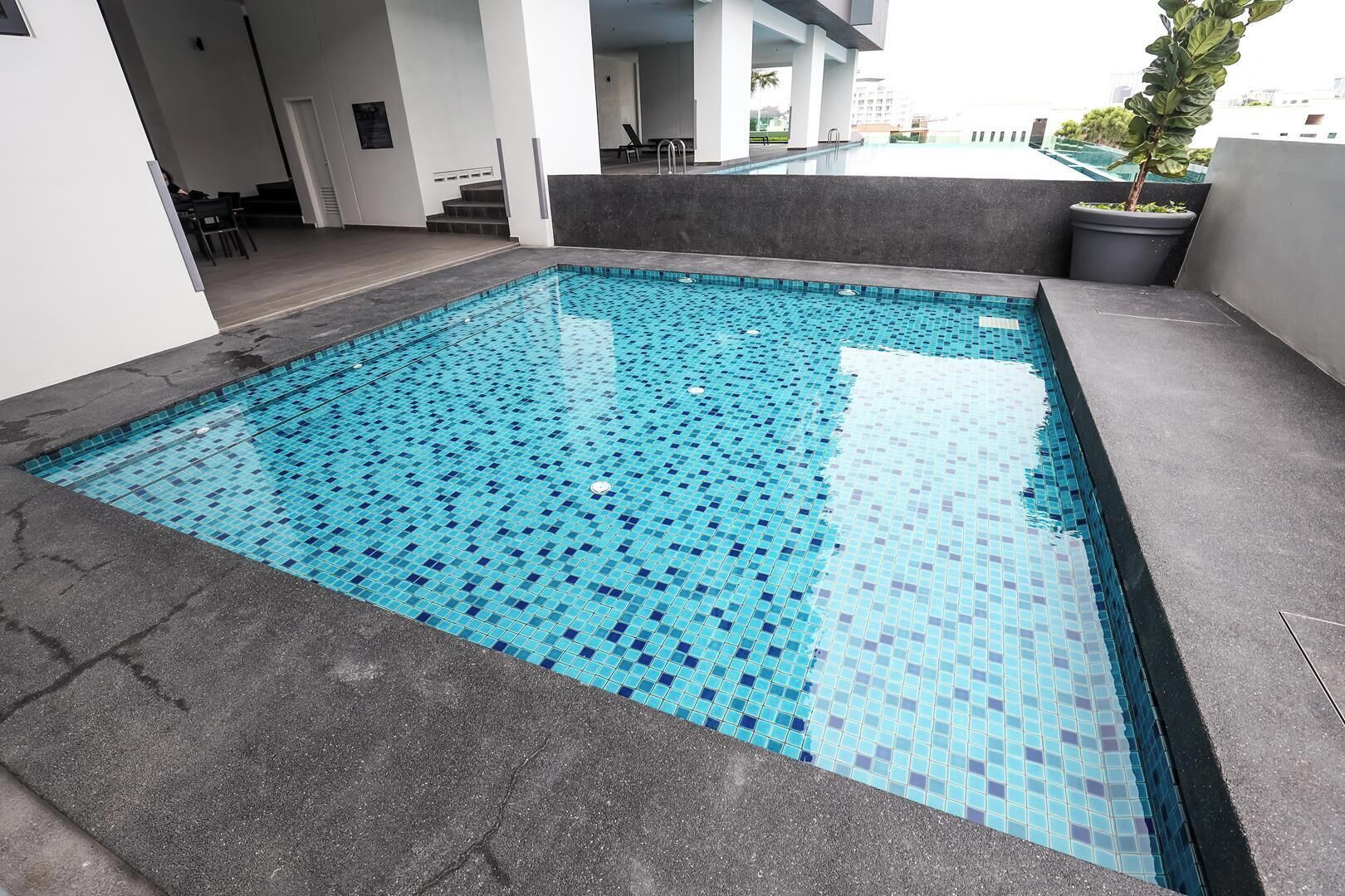 A rectangular outdoor swimming pool with blue mosaic tiles, surrounded by a dark grey floor.