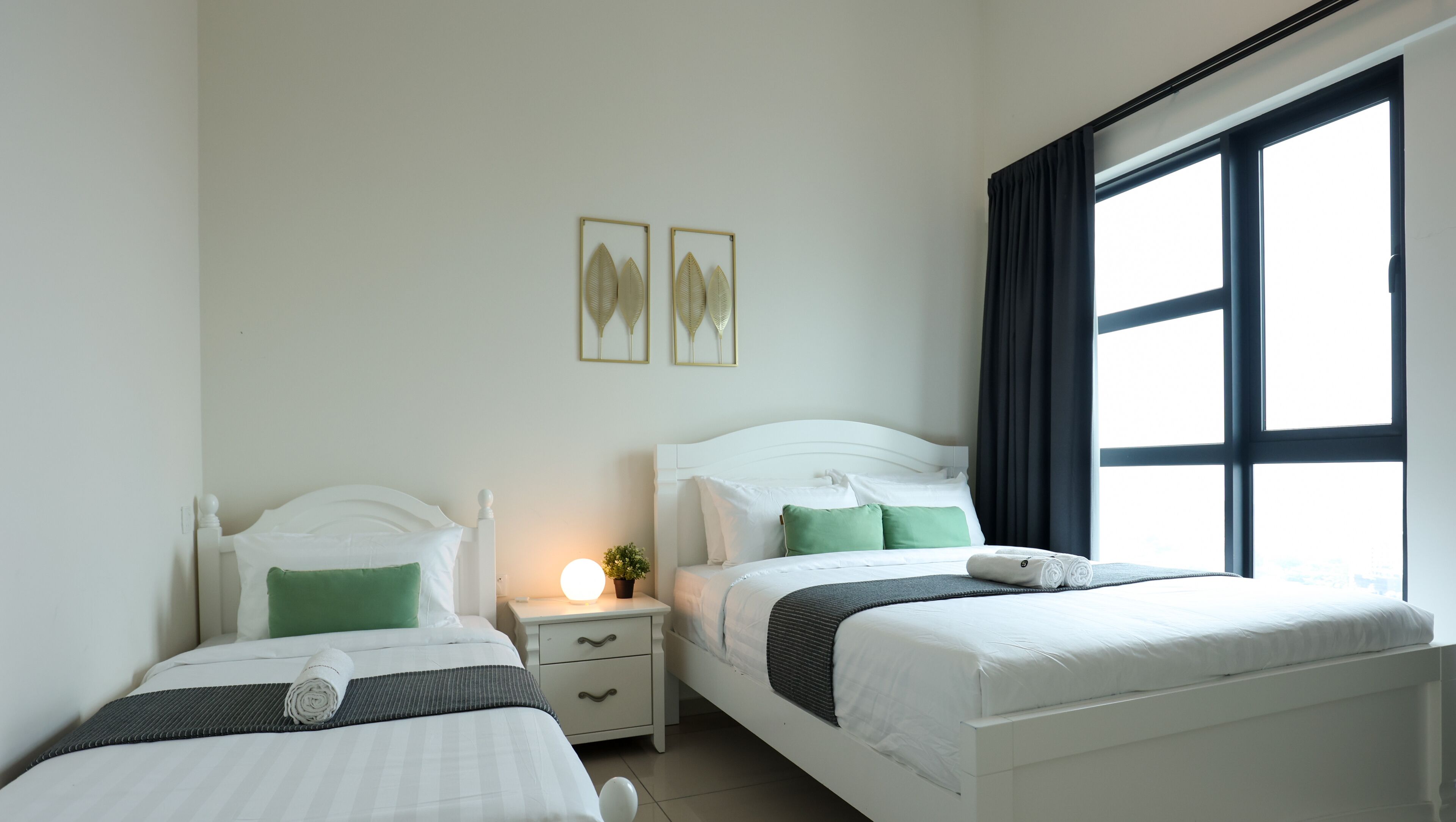 A hotel room with two beds, a nightstand, a lamp, and a window with curtains.