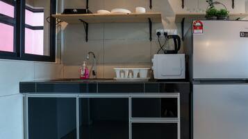 Een compacte keuken met een ingebouwde kookplaat, een spoelbak en een koelkast. Boven de kookplaat bevinden zich planken met pannen en een potplant.