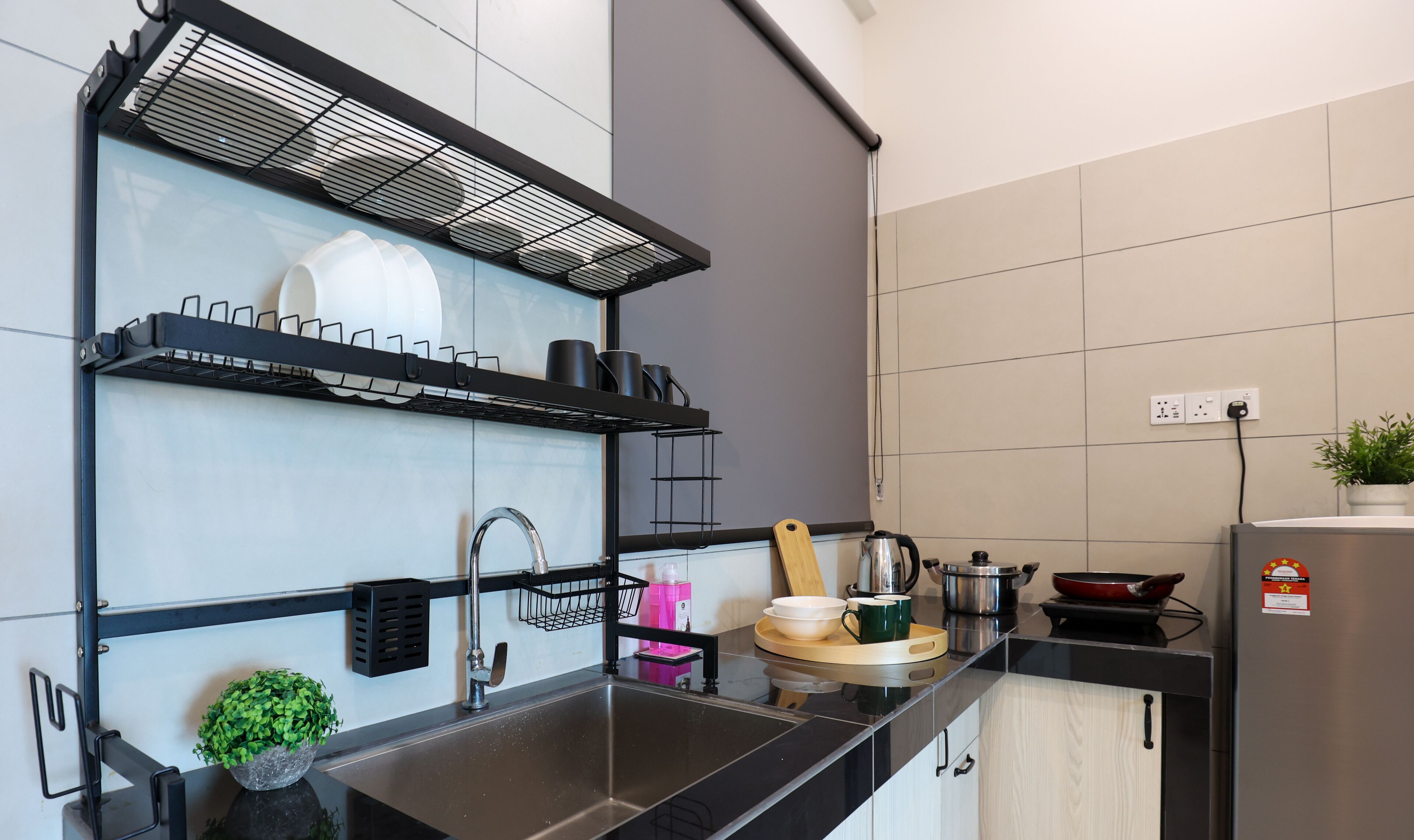 A modern kitchen with black countertops, a stainless steel sink, and a built-in oven. There are shelves above the sink holding dishes and cookware.