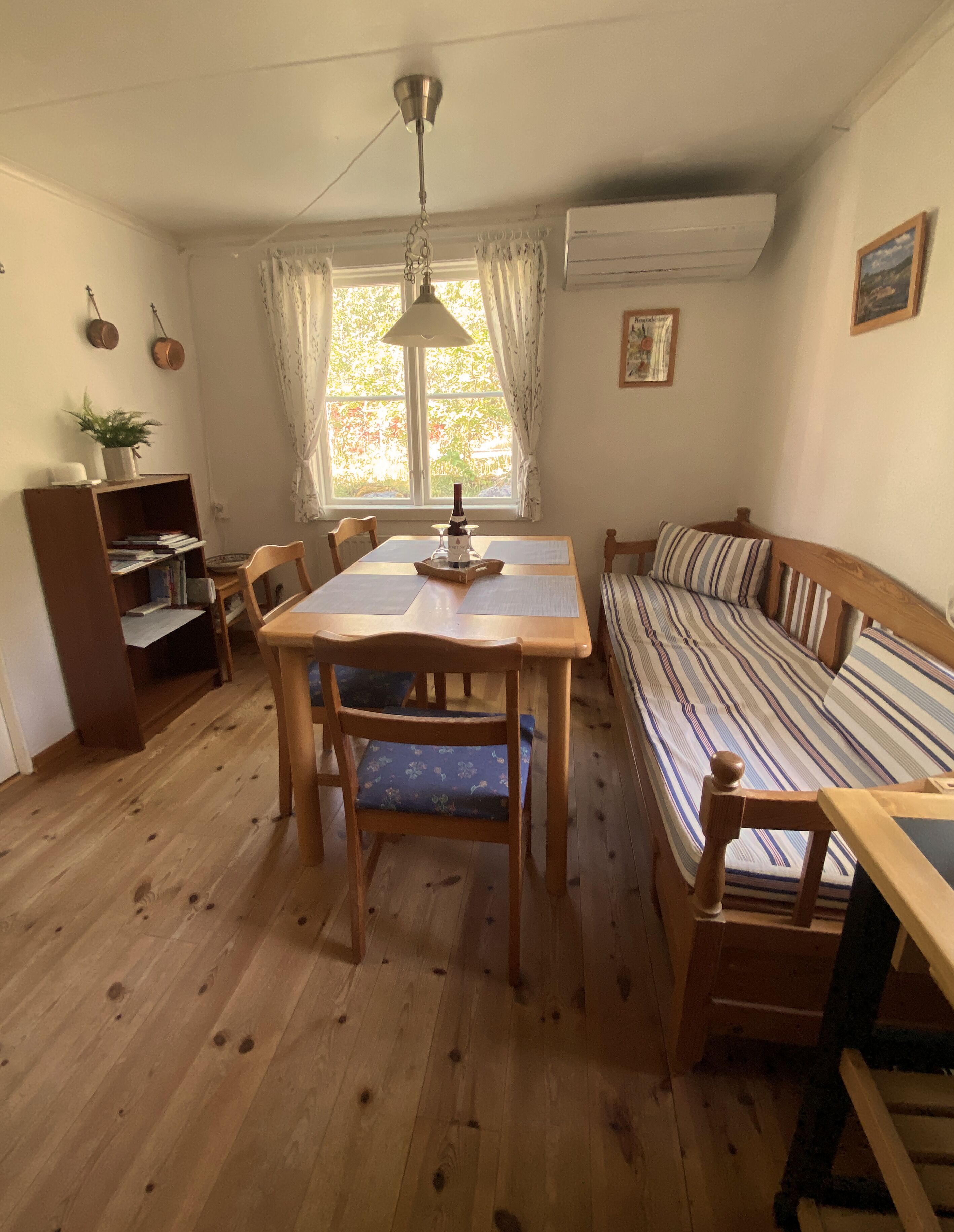 Une pièce chaleureuse avec une table à manger en bois, des chaises, un canapé, une bibliothèque et une fenêtre avec des rideaux.
