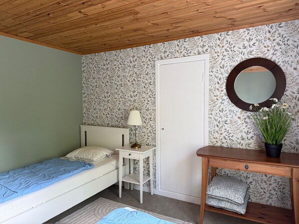A small, single-bed room with a wooden ceiling, a bedside table with a lamp, a mirror, and a potted plant. - Grimsebo Vacation Home in an idyllic, secluded setting—pure nature! (Kalmar län)
