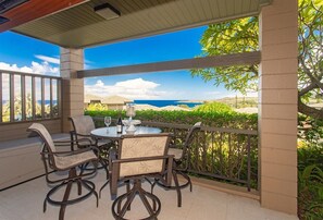 Une terrasse couverte avec une table et des chaises, une vue sur l’océan et une rambarde.