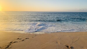 Una playa con huellas que conducen al agua, un cielo despejado y el sol poniéndose o saliendo.