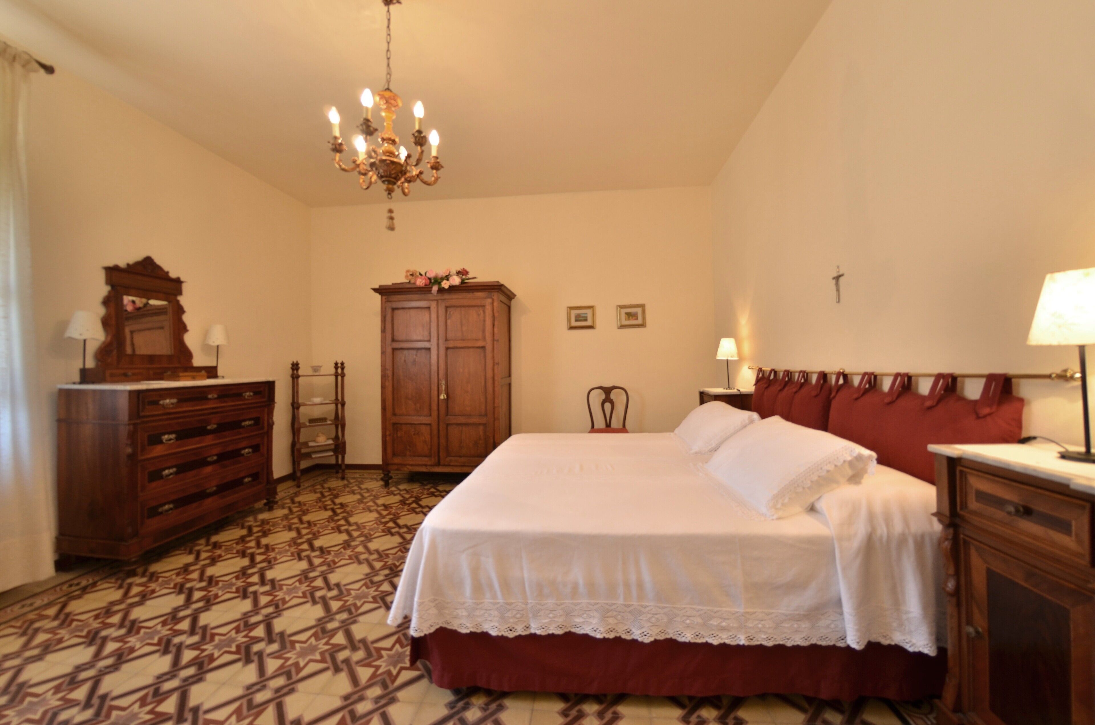 A bedroom with a large bed, wooden dresser, and a chandelier.