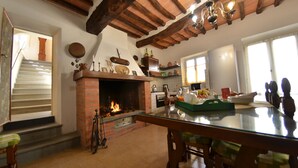 Una cocina con chimenea de ladrillo, vigas de madera y un comedor con mesa de vidrio.