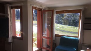 Ein Zimmer mit einem Bett, einem blauen Stuhl, einem Fenster mit Blick auf eine Wiese und einer zur Außenwelt führenden Tür.
