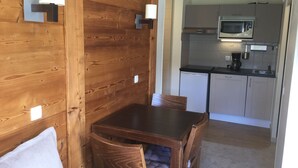 Ein Essbereich mit Holzwänden, einem Tisch und Stühlen, eine Küche mit Mikrowelle und Schränken sowie ein kleiner Kühlschrank.