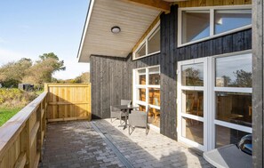 Relax in the serene outdoor patio, surrounded by lush greenery and trees, with a table for two and comfortable seating.