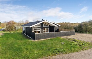 Cozy cabin with a pitched roof and large window, set amidst a grassy area with a wooden fence.