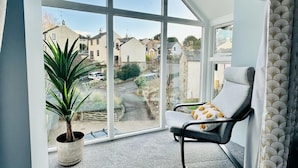 A room with a large window, a chair, and a potted plant. - Luxurious, Contemporary Detached Holiday Home on a quiet cul-de-sac (Kirkby Lonsdale)