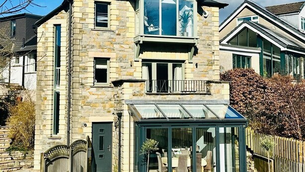 A two-story stone house with a conservatory, a visible balcony, and a gravel driveway. - Luxurious, Contemporary Detached Holiday Home on a quiet cul-de-sac (Kirkby Lonsdale)