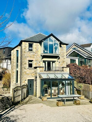 A two-story stone house with a conservatory, a visible balcony, and a gravel driveway. - Luxurious, Contemporary Detached Holiday Home on a quiet cul-de-sac (Kirkby Lonsdale)