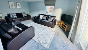 A living room with two sofas, a TV, and a window with curtains. - Luxurious, Contemporary Detached Holiday Home on a quiet cul-de-sac (Kirkby Lonsdale)