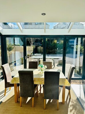 Un espace de repas moderne avec un patio vitré, une table dressée pour quatre personnes et une vue sur le jardin et la cour arrière.