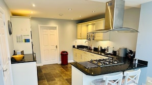 A modern kitchen with a central island, white cabinetry, and a stainless steel range hood. - Luxurious, Contemporary Detached Holiday Home on a quiet cul-de-sac (Kirkby Lonsdale)