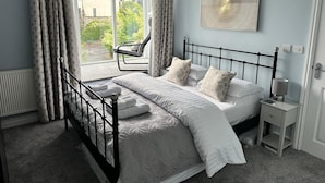 A bedroom with a bed, a chair, a nightstand, and a window with curtains. - Luxurious, Contemporary Detached Holiday Home on a quiet cul-de-sac (Kirkby Lonsdale)