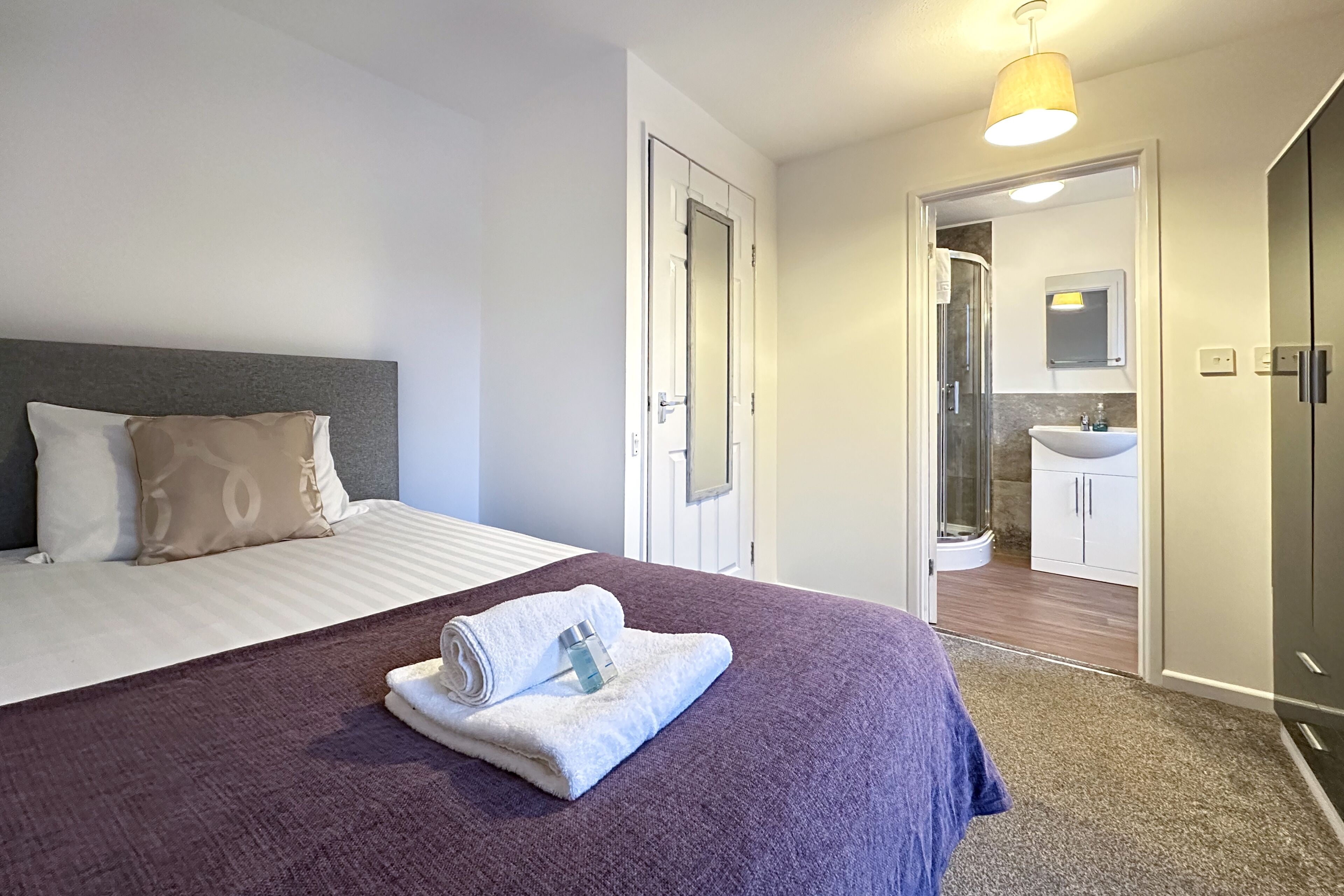 A hotel room with a bed, a bathroom visible through an open door, and a shower area.