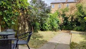 A patio with a table and chairs, surrounded by greenery and a house in the background.