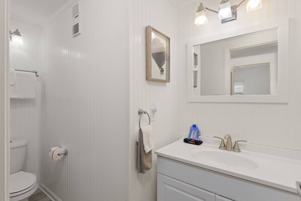 A bathroom with a toilet, a sink, a mirror, and a towel rack. - Oceanfront 1BR Condo | Private Balcony, Direct Beach Access, Sleeps 4 (Jacksonville Beach)