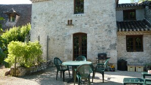 A stone building with a tiled roof, a small porch, and a gravel patio with green chairs and a table. - luxury cottage for adult couples, peaceful, unobstructed views, large swimming pool (Boisse, France)