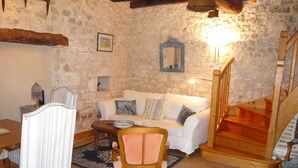 A stone-walled living room with a white sofa, a wooden chair, a dining table, and a staircase. - luxury cottage for adult couples, peaceful, unobstructed views, large swimming pool (Boisse, France)