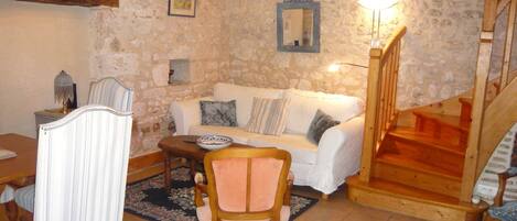 A stone-walled living room with a white sofa, a wooden chair, a dining table, and a staircase.