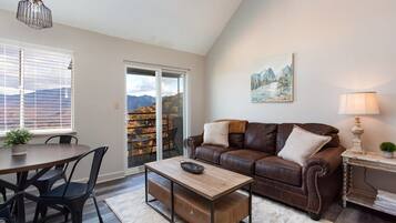 A living room with a brown leather sofa, a wooden coffee table, a dining table with chairs, and a view through a sliding glass door.