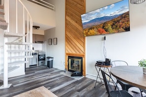 A modern kitchen with a fireplace, a dining area with a table and chairs, and a staircase leading to an upper level. - Sweeping Views Of GSMNP/Indoor Pool & Hot Tub (Gatlinburg)
