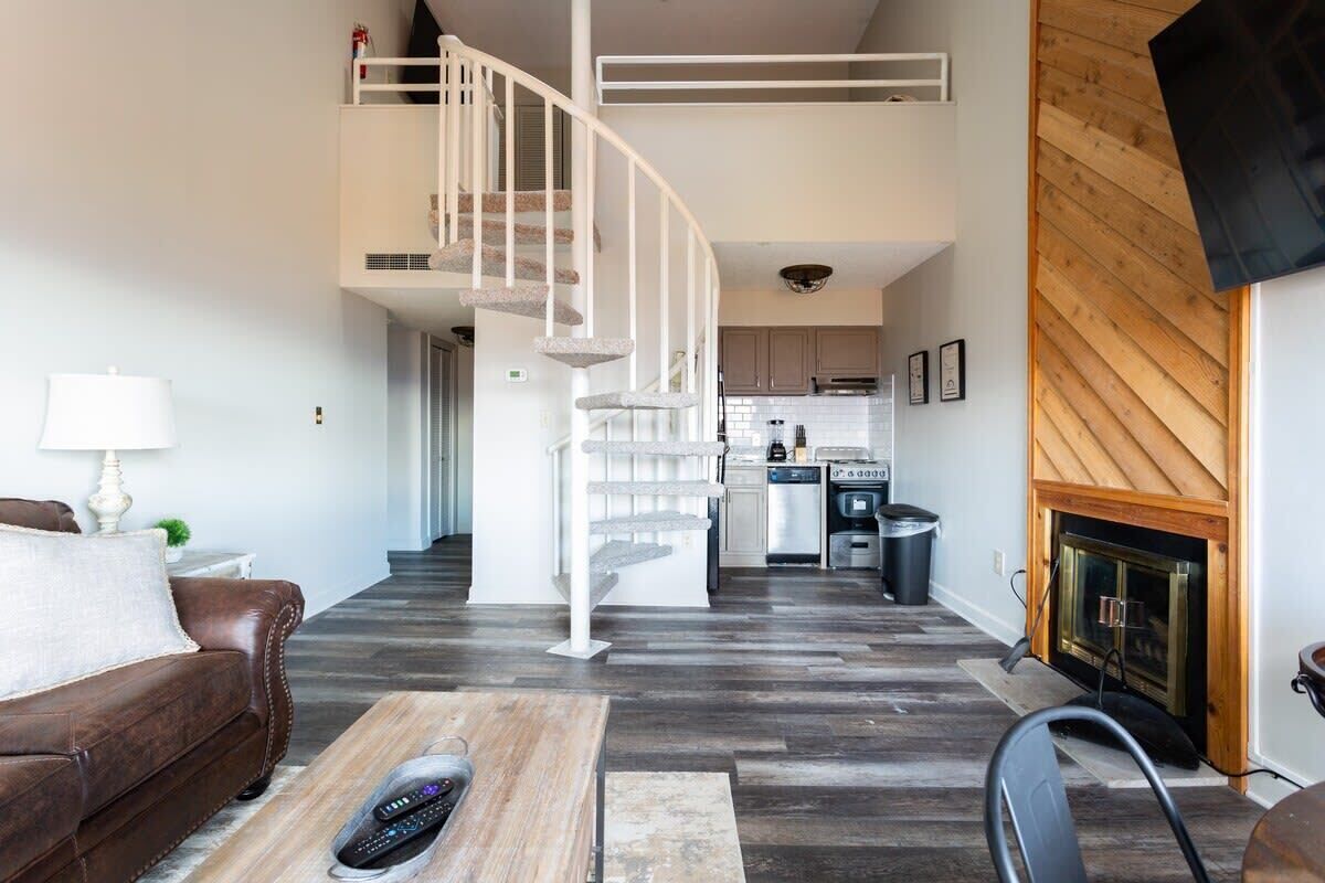 A living room with a brown leather sofa, a wooden coffee table, a white spiral staircase, and a kitchen in the background.
