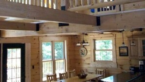 Eine geräumige Holzhütte mit hohen Decken, Holzbalken, einem Essbereich und einem Balkon.