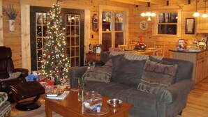 Ein gemütliches Blockhaus-Interieur mit Wohnzimmer, Essbereich und Küche. Im Wohnzimmer steht ein Weihnachtsbaum.