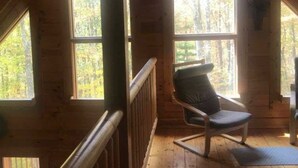 Eine Holzhütte mit geneigtem Dach, großen Fenstern und einem Stuhl am Fenster.