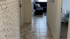 Un pasillo con pared de ladrillo blanco, suelo de baldosas y un sofá oscuro al fondo.