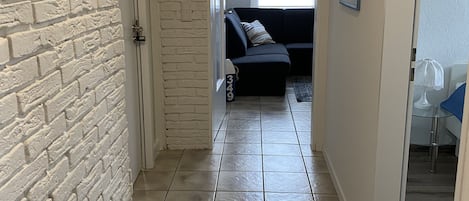 En hall med en vit tegelvägg, ett kaklat golv och en mörkfärgad soffa i bakgrunden.