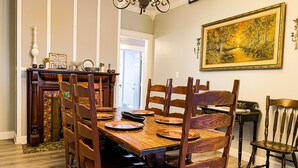 A dining area with a wooden table set for six, surrounded by six chairs. A fireplace with a mantel is visible to the left.