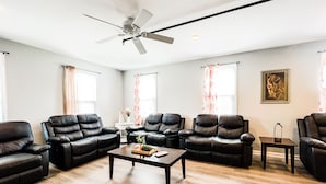 A spacious living room with leather sofas, a coffee table, and a ceiling fan.