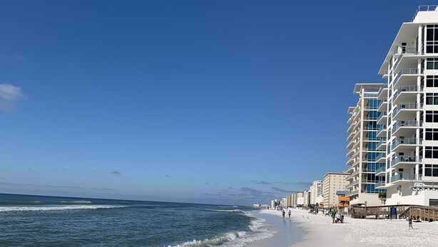A beach with a clear sky, a sandy shore, and a building with multiple floors and balconies. - Relax near Destin Beach. Destin’s best resort style condo! (Destin)