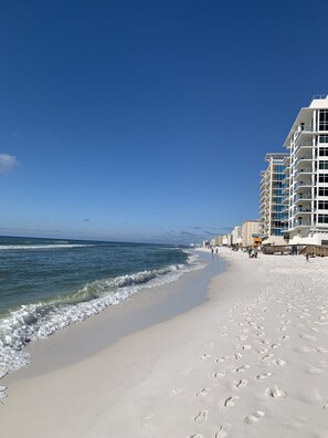 A beach with a clear sky, a sandy shore, and a building with multiple floors and balconies.