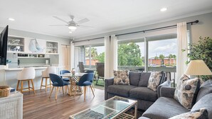 A modern living room with a grey sofa, blue chairs, a glass coffee table, and a ceiling fan. - Relax near Destin Beach. Destin’s best resort style condo! (Destin)