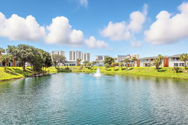 A lake with a fountain, surrounded by buildings and greenery.