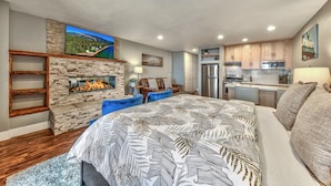 A modern bedroom with a fireplace, a large bed, a desk, and a kitchenette. - Lakeland Village #225 - Studio in Lodge, romantic remodel (South Lake Tahoe)