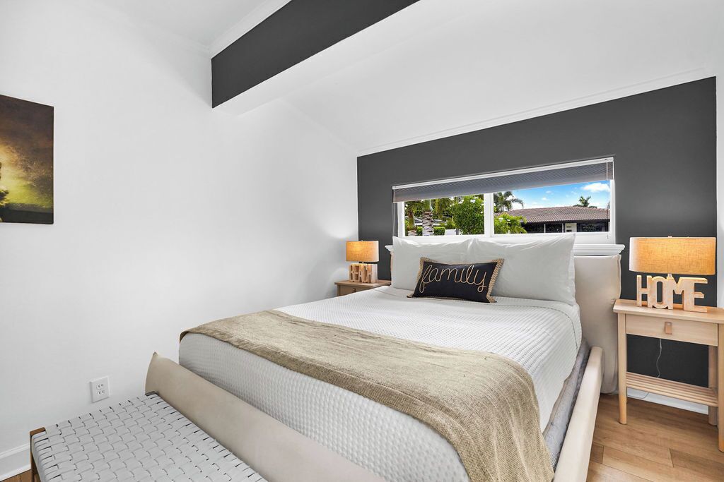 A modern bedroom with a large bed, a window with a view, and a bedside table with a lamp.