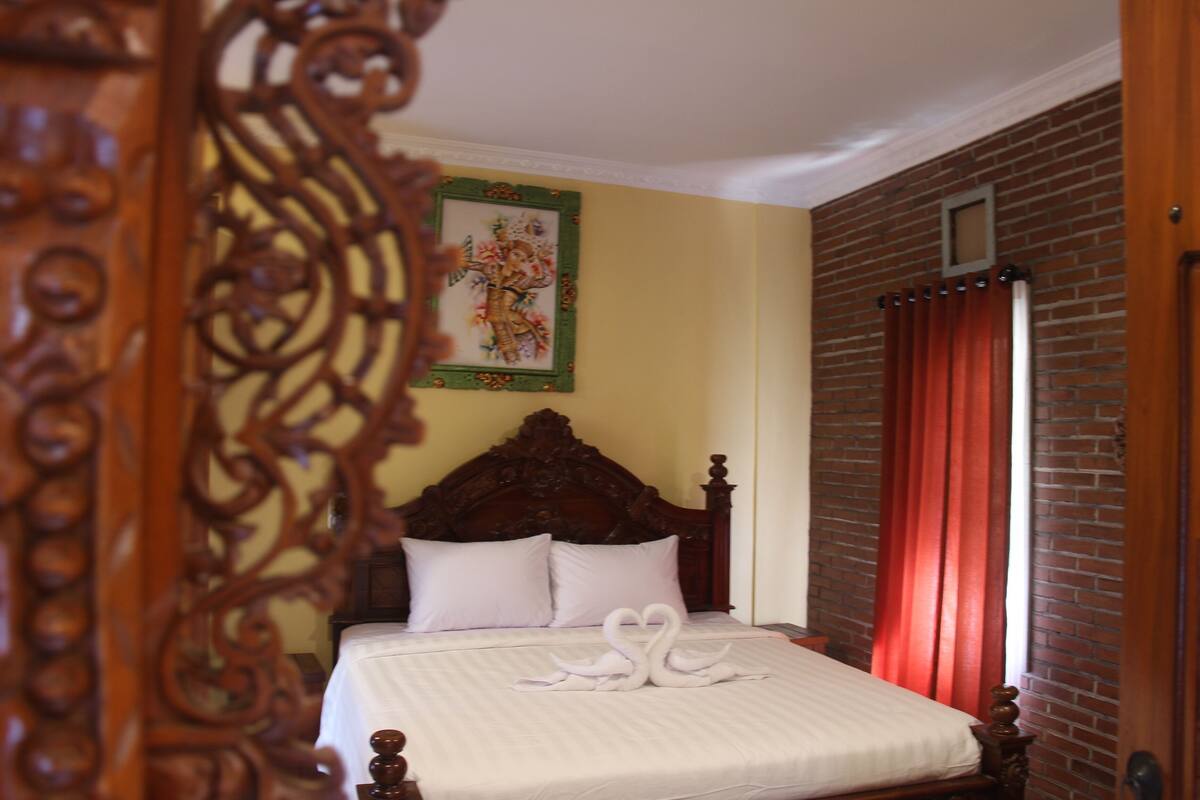 A neatly made bed with a white bedspread and two pillows, a wooden headboard, a red curtain, and a framed picture on the wall.