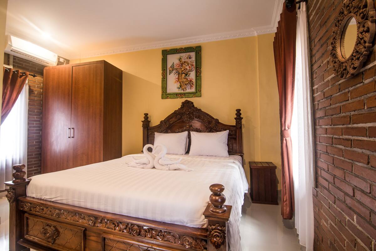 A neatly made bed with white linens and decorative swan pillows, a wooden headboard, and a framed artwork above it.