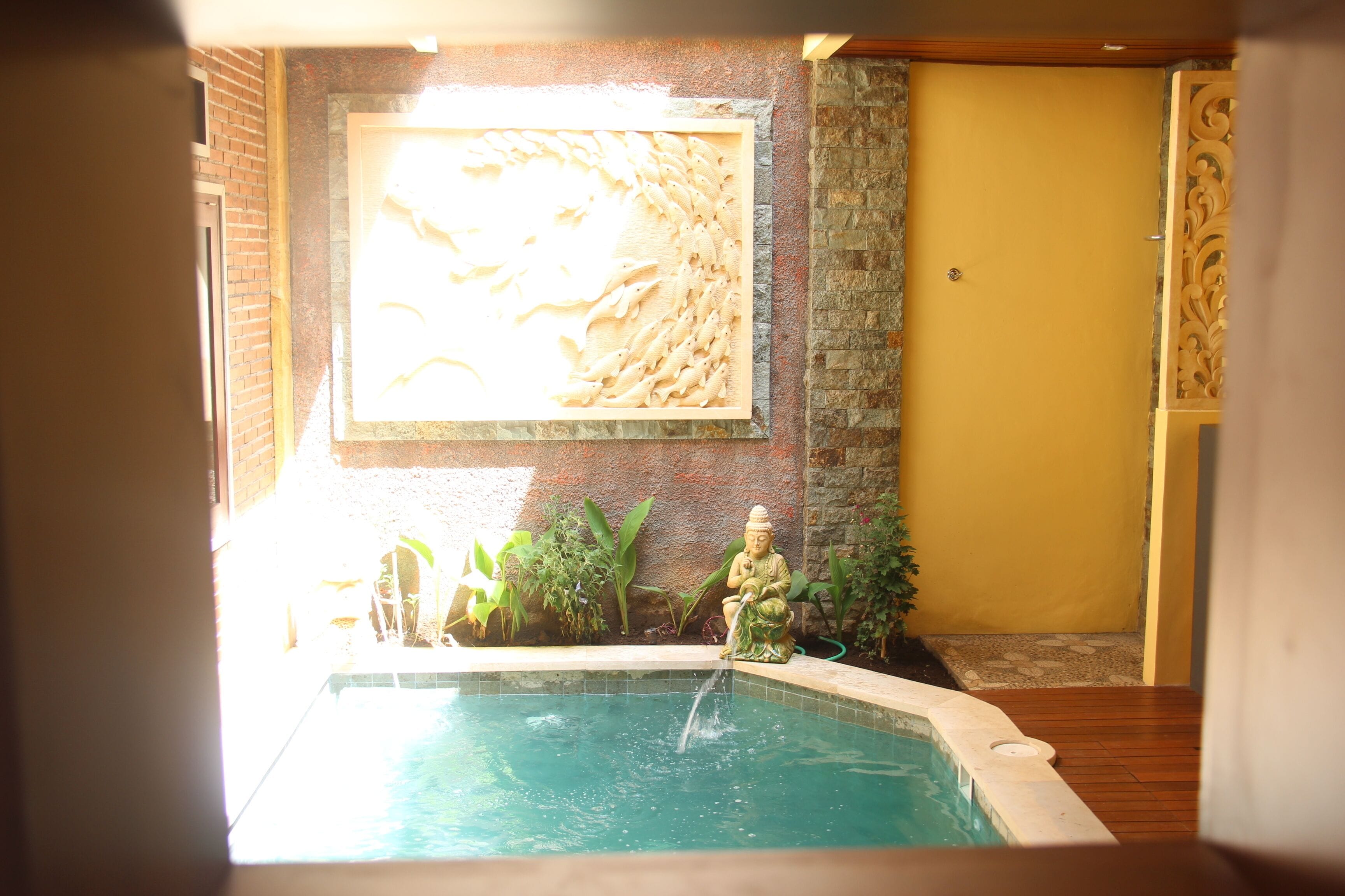 A pool with a statue, a yellow door, and a wall with a relief sculpture.