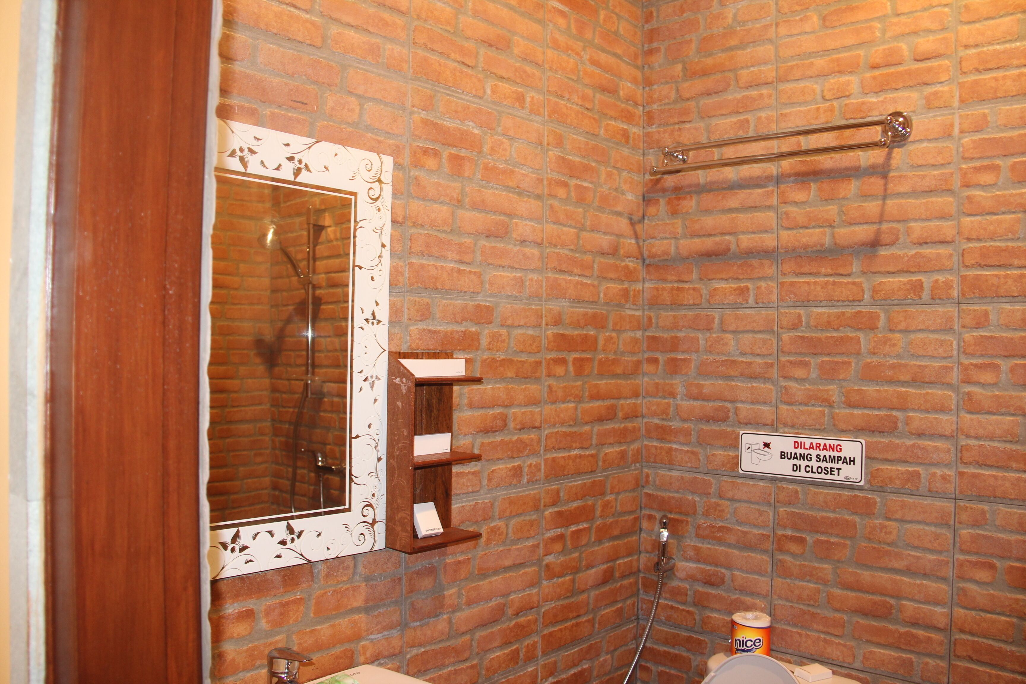 A bathroom with a brick wall, a wooden-framed mirror, a towel rack, and a sign indicating a closet.