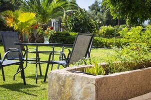 A garden area with a table and chairs, surrounded by lush greenery and palm trees.