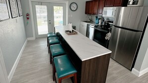 A modern kitchen with a central island, stainless steel appliances, and teal bar stools.